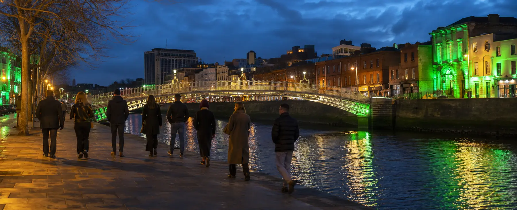 Neuf piétons près de la Liffey et du Ha’penny Bridge éclairé en vert